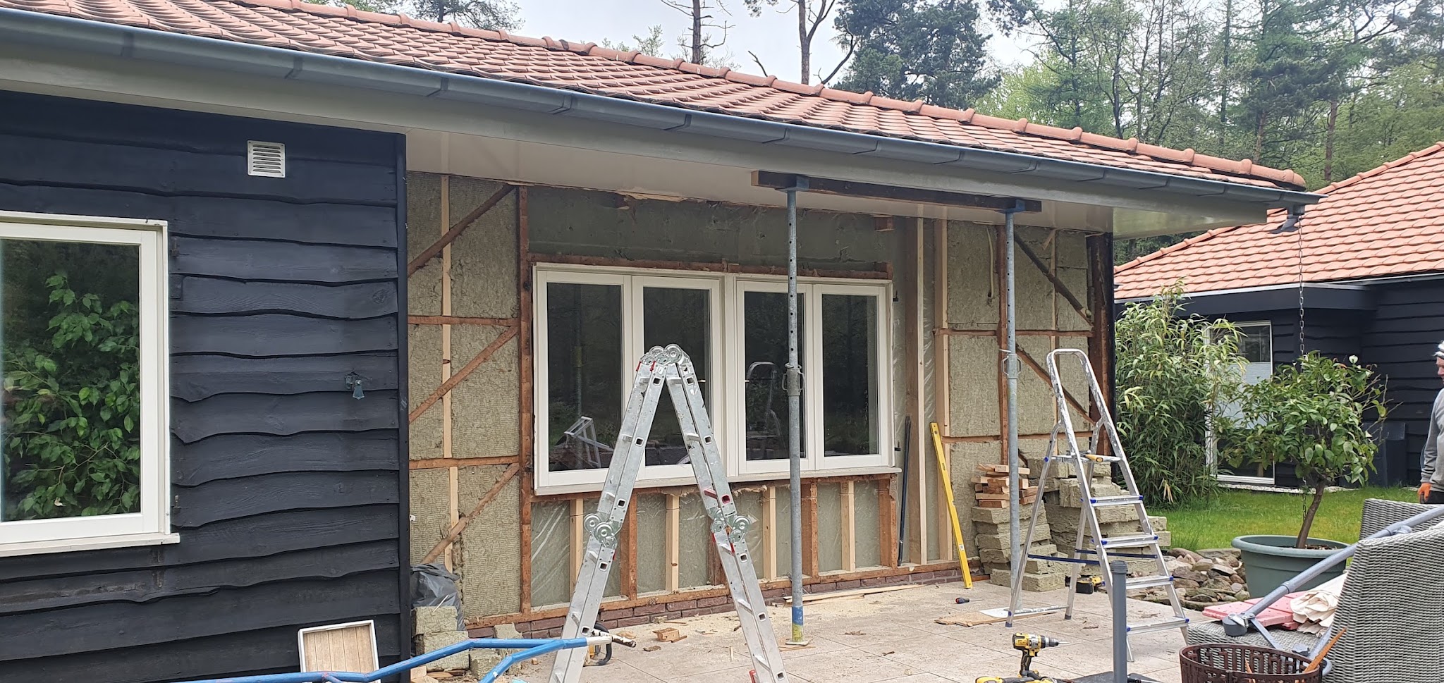 Verbouwing van een zwart houten huis: nieuwe kozijnen geplaatst in de aanbouw, ladders en isolatie nog in beeld