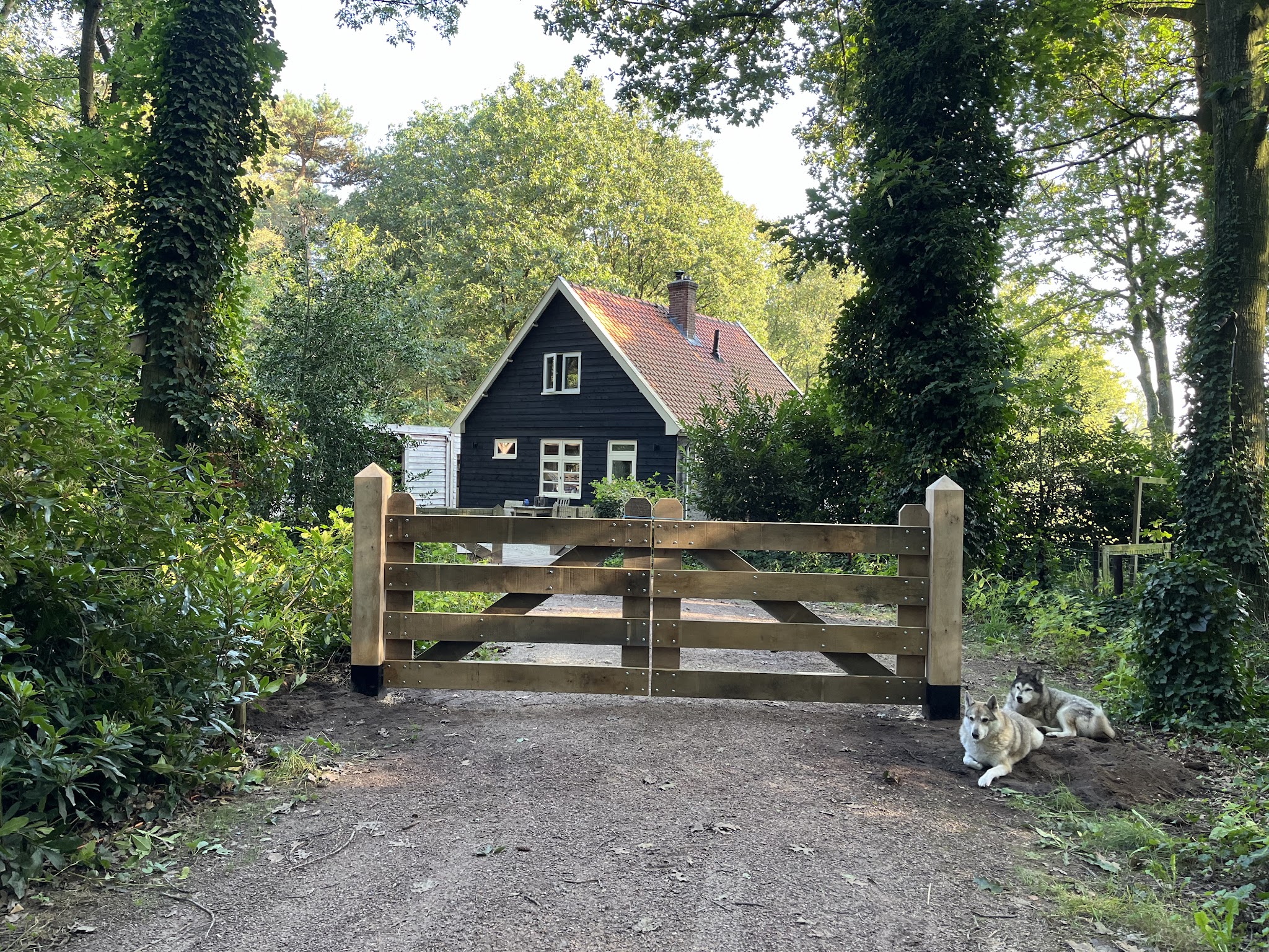Eiken poort tussen twee eiken palen op een bosrijk erf, twee husky's liggen ernaast