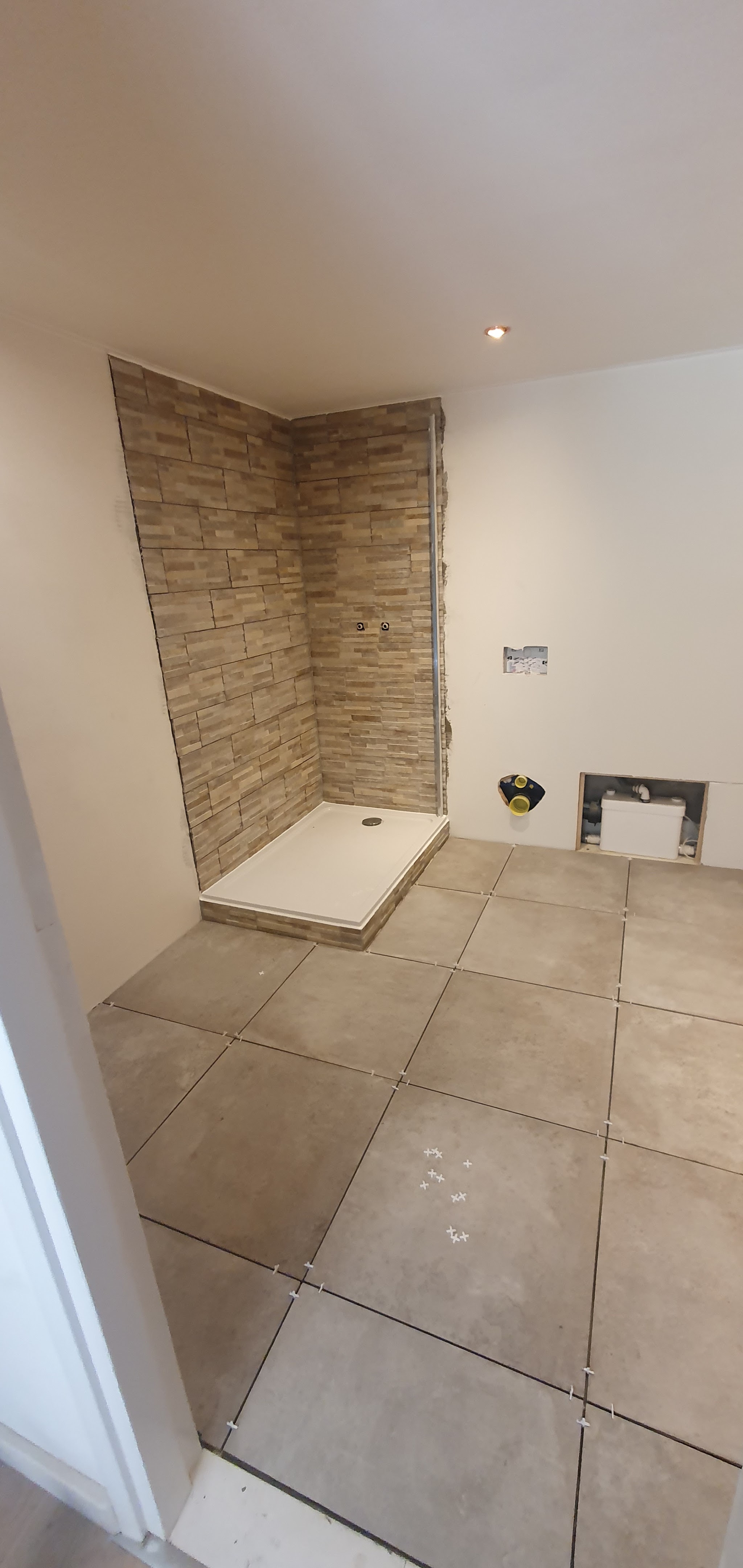 Badkamer in aanbouw: douchewand van steenstrips, douchebak en grote vloertegels met kruisjes